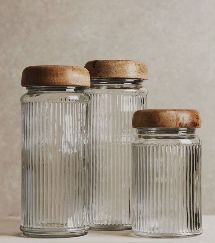 Three ribbed glass storage jars with wooden lids on a stone ledge